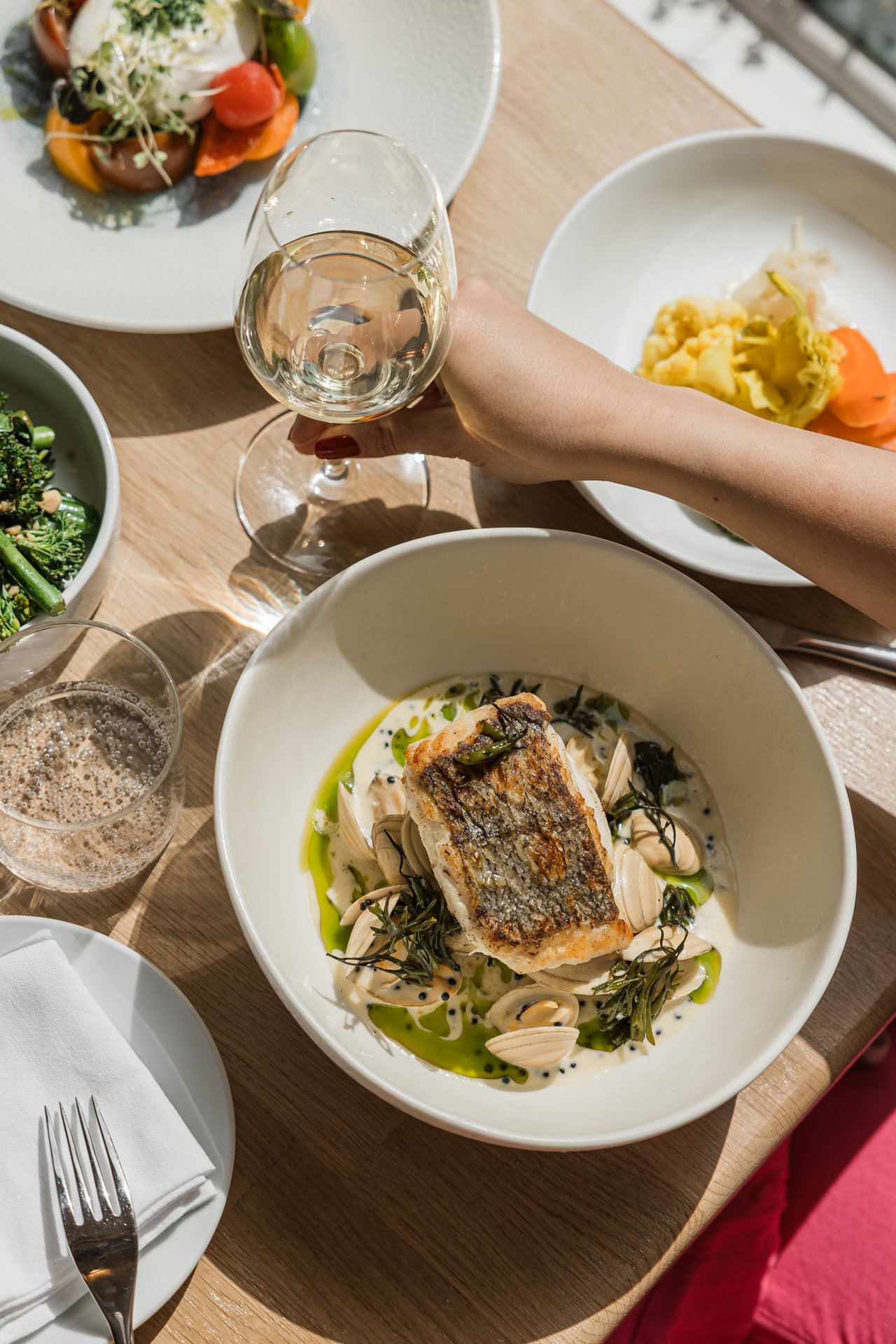 Hake with cockles in beurre blanc, a glass of white wine raised above the table