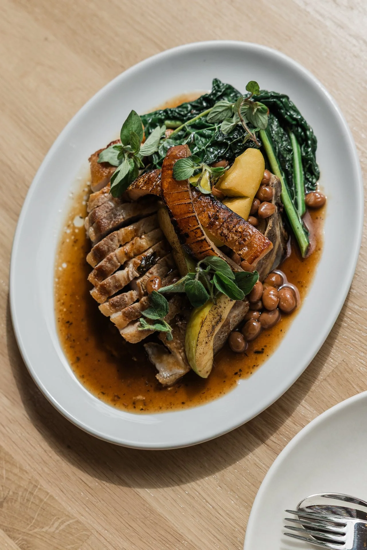 Pork chop with borlotti beans, cavolo nero and roast apple, served on an oval plate