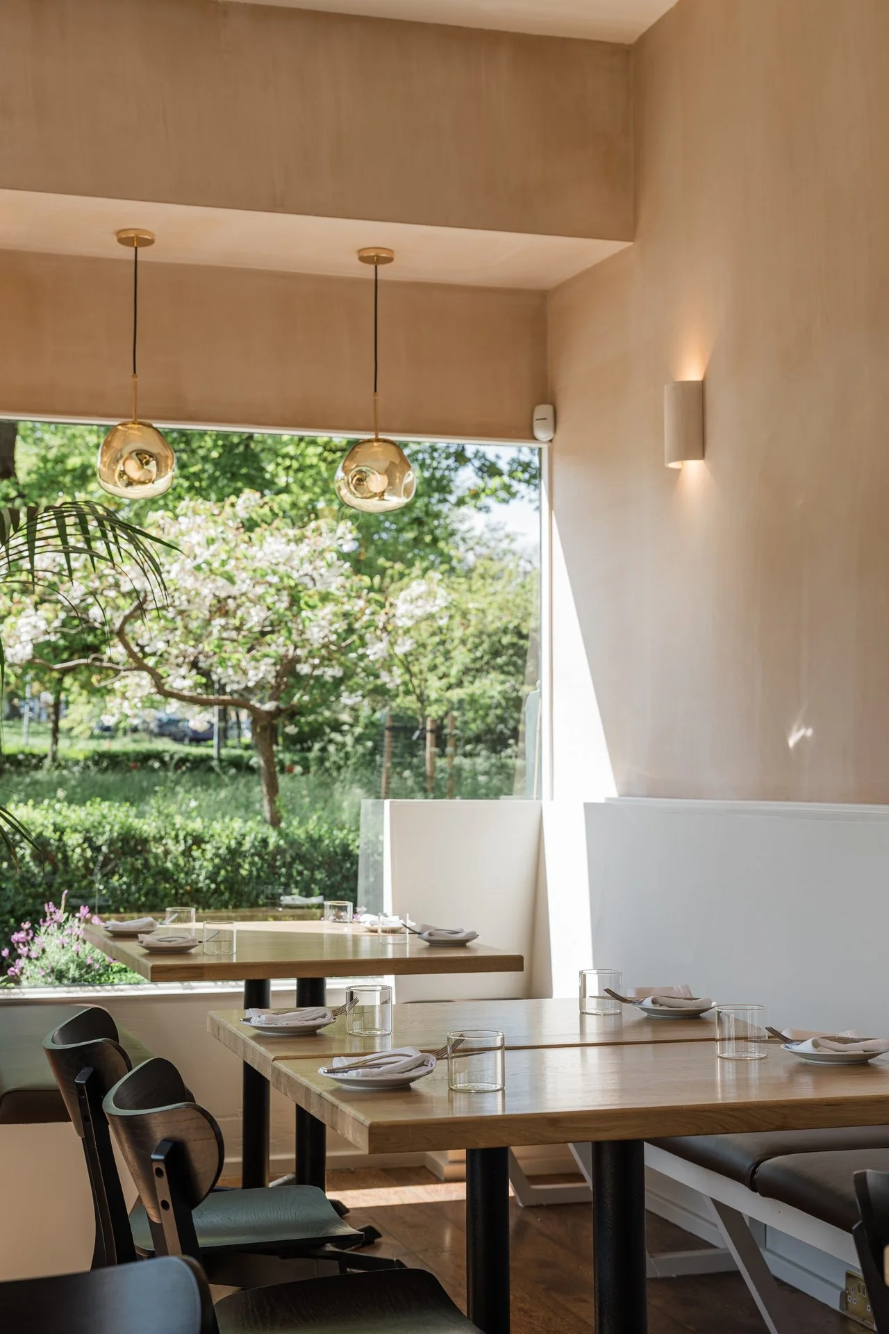 A booth beside Leftfield's picture window — gold pendant lights, warm plaster walls, cherry blossom on the Links beyond